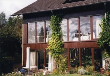 Außenansicht Modernes zweistöckiges Haus mit großen Fenstern, umgeben von üppigem Grün und Kletterpflanzen.