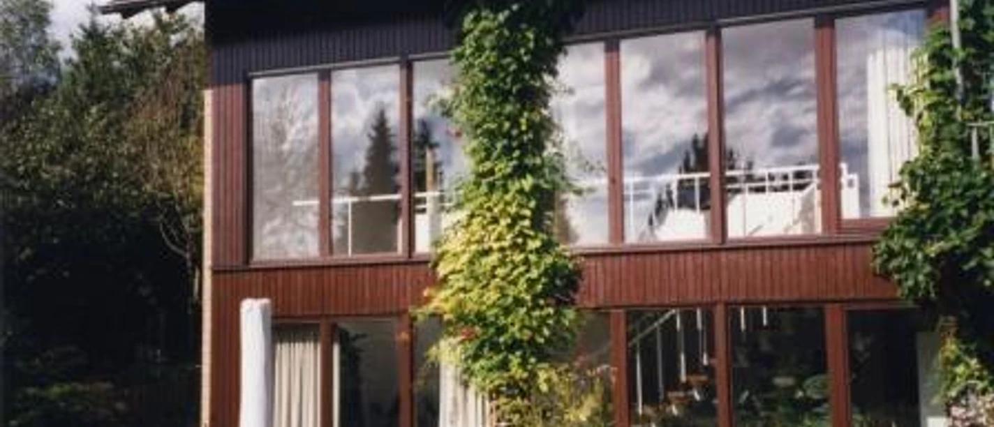 Außenansicht Modernes zweistöckiges Haus mit großen Fenstern, umgeben von üppigem Grün und Kletterpflanzen.