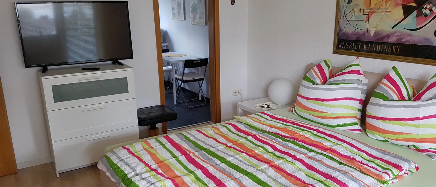 Ferienwohnung Schmitz Helles Schlafzimmer mit Doppelbett in bunter Streifenbettwäsche, Kommode und Flachbildfernseher.