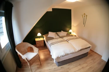 Gemütliches Schlafzimmer mit Doppelbett, zwei Nachttischen, Lampen und einem Korbstuhl.