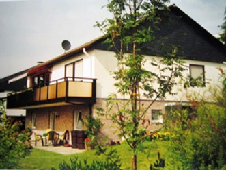 Außenansicht Zweistöckiges Haus mit Balkon, weiße Fassade, umgeben von Garten mit Bäumen und Sträuchern.