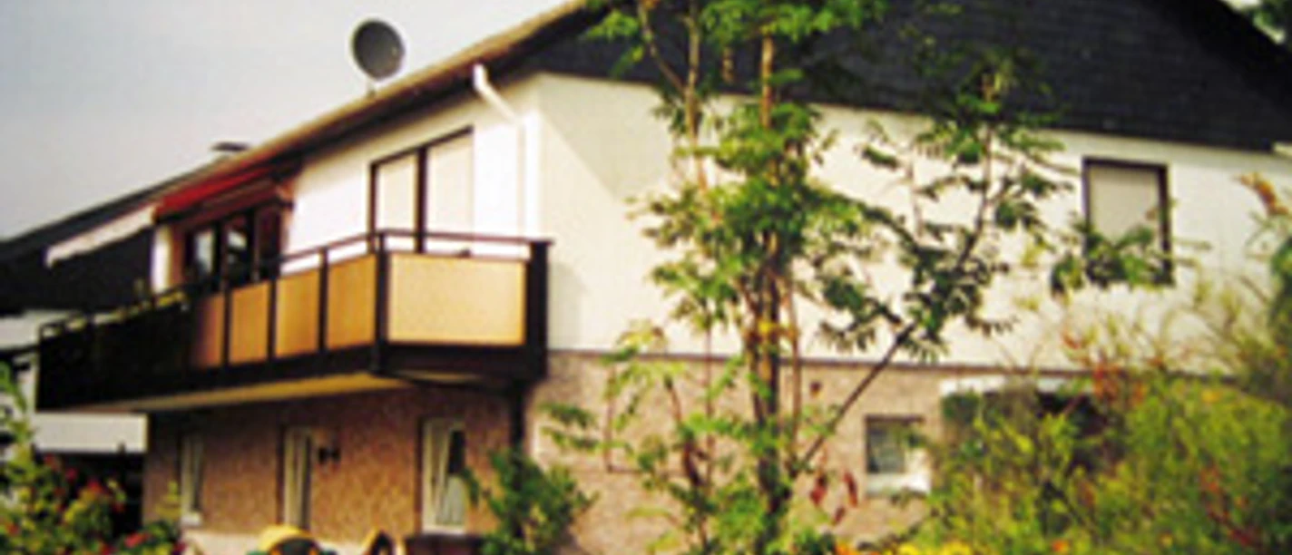 Außenansicht Zweistöckiges Haus mit Balkon, weiße Fassade, umgeben von Garten mit Bäumen und Sträuchern.