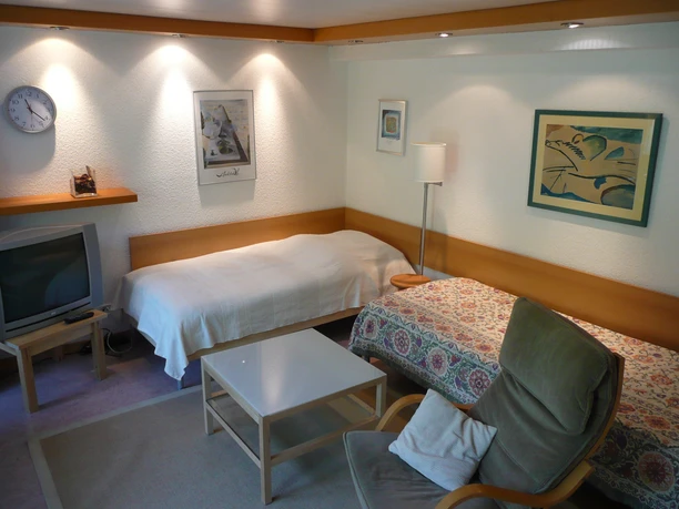 Schlafzimmer Gemütliches Wohnzimmer mit einem Einzelbett, einem Sessel und einem Fernseher in einem einladenden Ambiente.