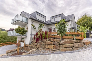 Außenansicht Zweistöckiges Haus mit modernem grauem Dach, Balkon, Steingarten und gepflegten Pflanzen im Vorgarten.