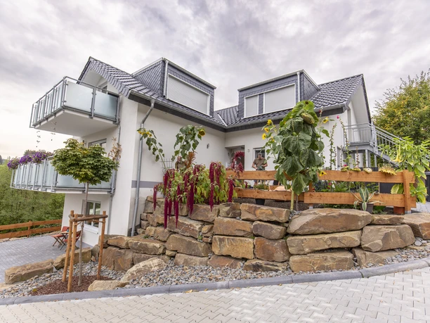 Außenansicht Zweistöckiges Haus mit modernem grauem Dach, Balkon, Steingarten und gepflegten Pflanzen im Vorgarten.