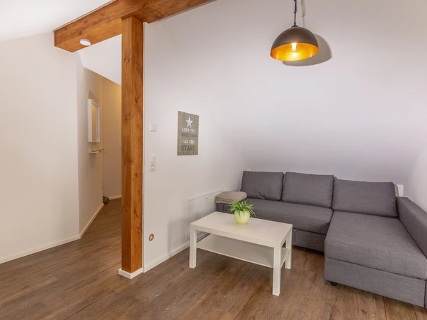 Mediendatei Gemütliches Wohnzimmer mit grauem Ecksofa, Holzboden, weißem Couchtisch und hängender Lampe.