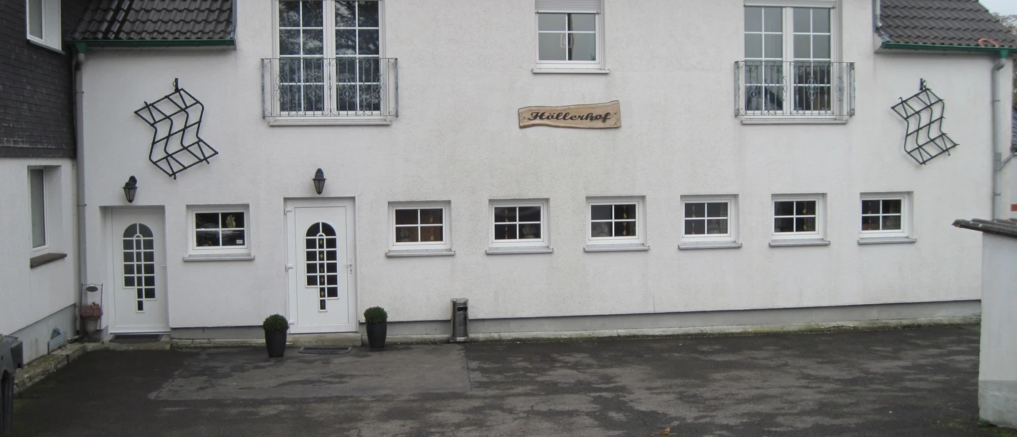 Höller Hof Weißes zweistöckiges Gebäude mit symmetrischem Design, zentralem Eingang und dekorativen Fenstern.