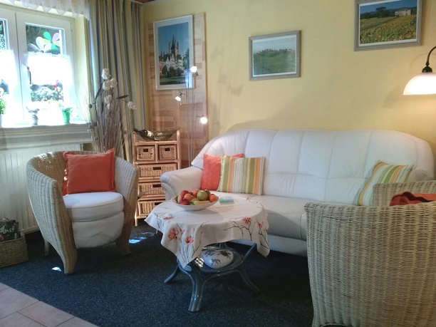 Ferienwohnungen Schulte Gemütliches Wohnzimmer mit weißen Möbeln, hellen Kissen und Tisch mit Obstschale in sonniger Atmosphäre.