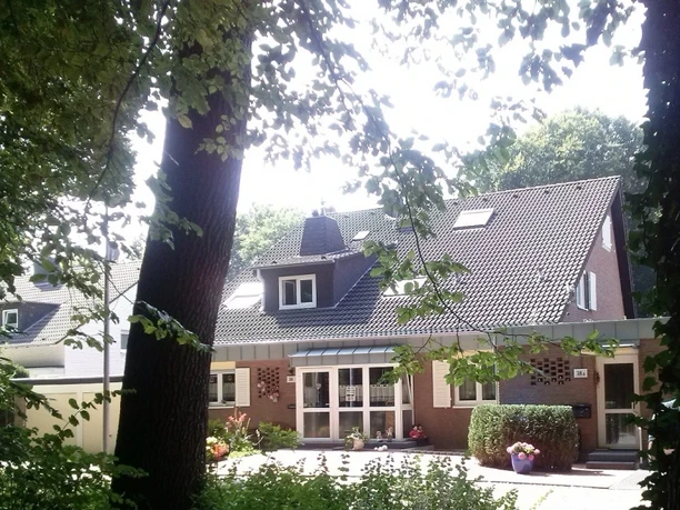 Ferienwohnungen Schulte Gemütliches einstöckiges Backsteinhaus im Grünen mit großen Fenstern, umgeben von Bäumen und Pflanzen.