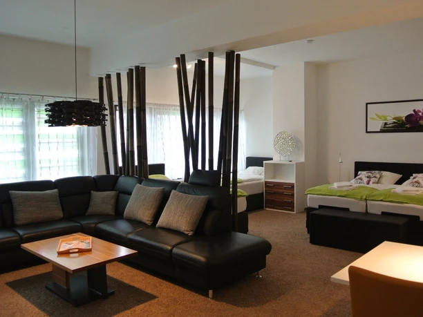 Gästehaus beim Prinz Modern eingerichtetes Apartment mit schwarzen Sofas, Holztisch und zwei Einzelbetten im Hintergrund.