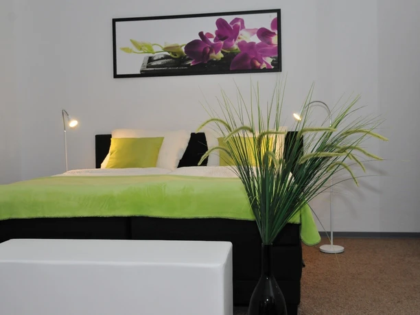 Gästehaus beim Prinz Ein modernes Schlafzimmer mit grün-weißem Farbschema, Doppelbett, Nachttischlampen und Pflanzen.