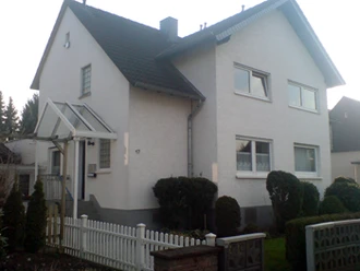Außenansicht Zweistöckiges Einfamilienhaus mit Satteldach, weißer Fassade und gepflegtem Vorgarten.