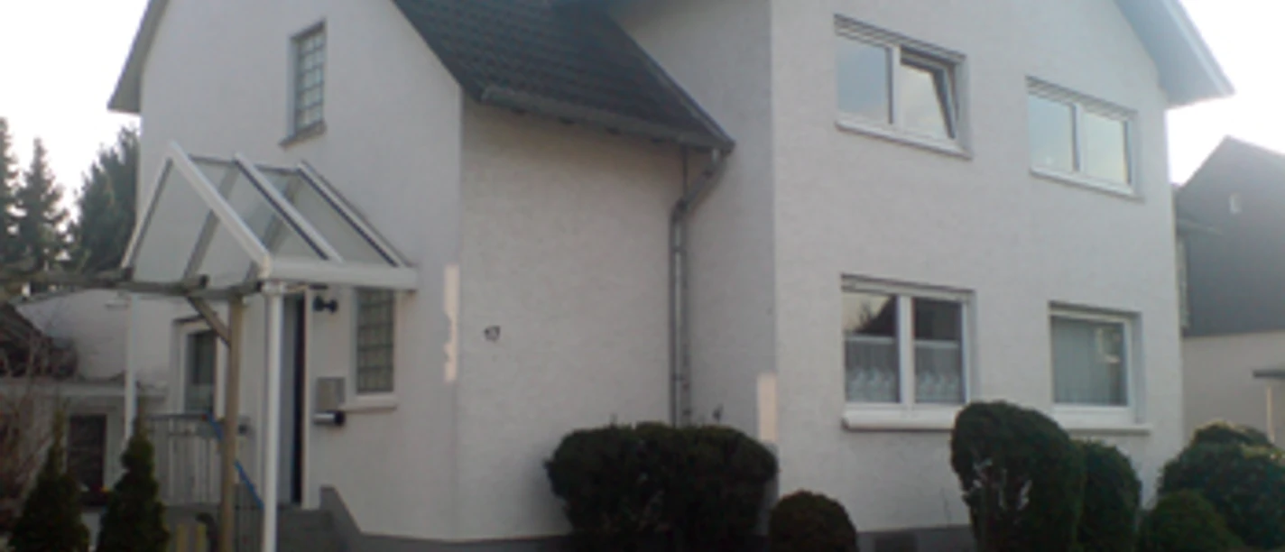 Außenansicht Zweistöckiges Einfamilienhaus mit Satteldach, weißer Fassade und gepflegtem Vorgarten.