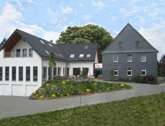 Außenansicht Zwei moderne Gebäude mit Schieferdächern, Blumenbeet im Vordergrund, klarer Himmel im Hintergrund.