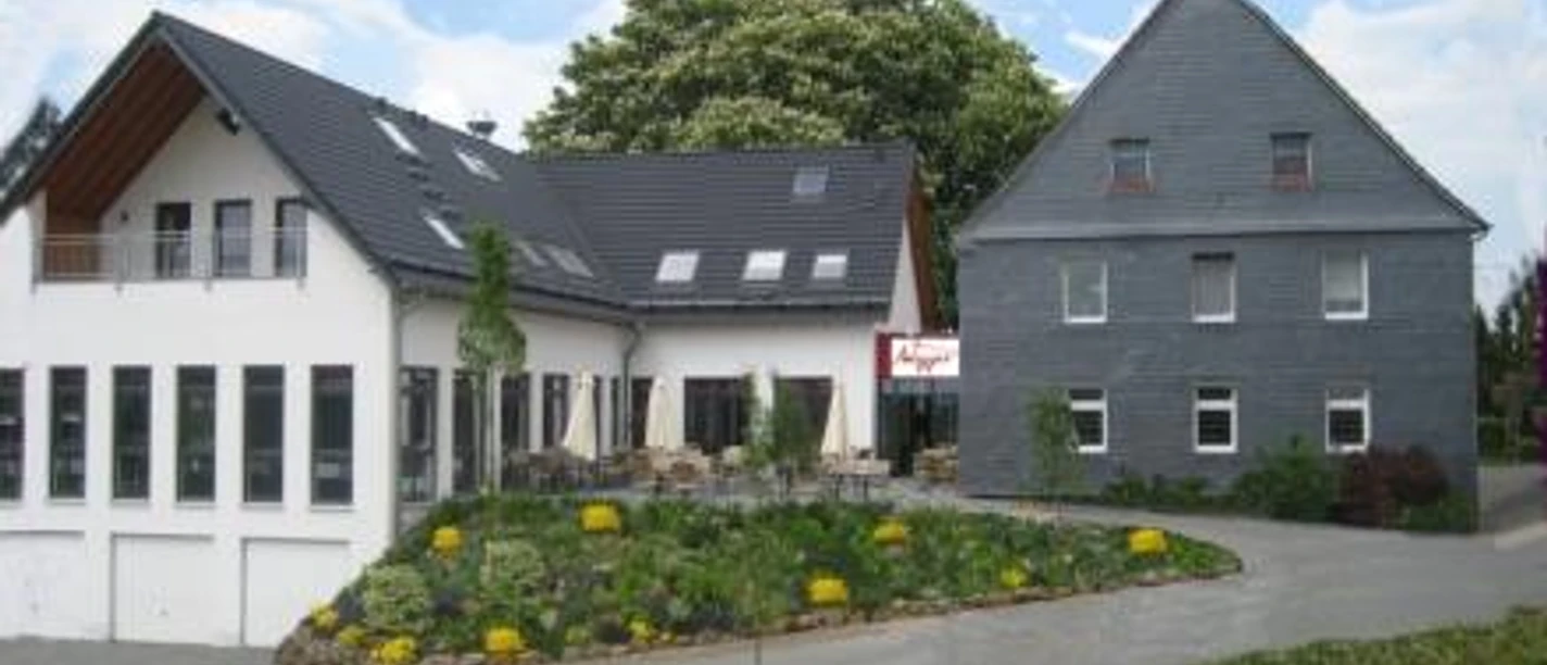 Außenansicht Zwei moderne Gebäude mit Schieferdächern, Blumenbeet im Vordergrund, klarer Himmel im Hintergrund.