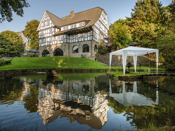 Blick auf Haus Varresbeck Fachwerkhaus mit Gartenpavillon spiegelt sich im ruhigen Wasser eines kleinen Teiches wider.