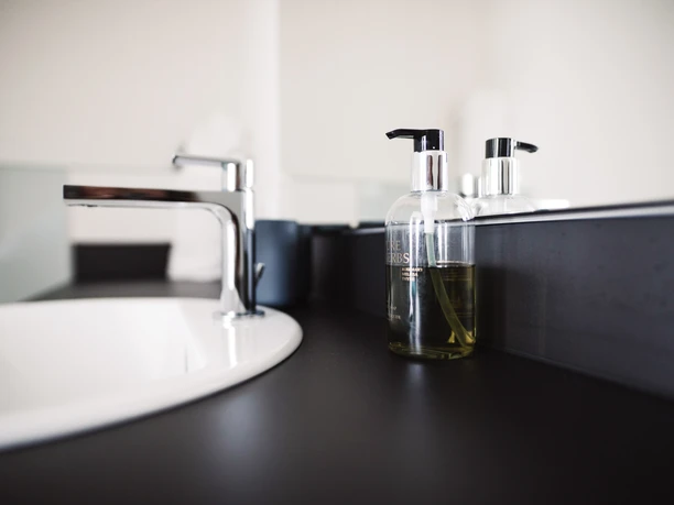 Badezimmer Modernes Waschbecken mit glänzendem Wasserhahn und Seifenspender auf dunkler Ablagefläche.