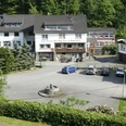 Haus am Mühlenberg Gasthof in ländlicher Umgebung mit Parkplatz, umgeben von Bäumen, und einem Brunnen im Vordergrund.