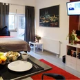 Wohnraum Wohnung A Modernes Apartment mit Doppelbett, TV, Esstisch, Obstschale und Stadtbild an der Wand.