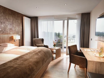 Zimmerbeispiel Modern eingerichtetes Hotelzimmer mit Doppelbett, Schreibtisch, TV, offenem Fenster und Sitzbereich.