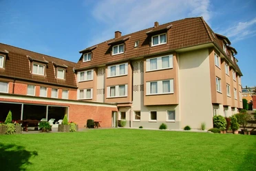 Hotel Fettehenne Dreistöckiges Gebäude mit braunem Dach und hellem Putz, umgeben von gepflegtem Garten.