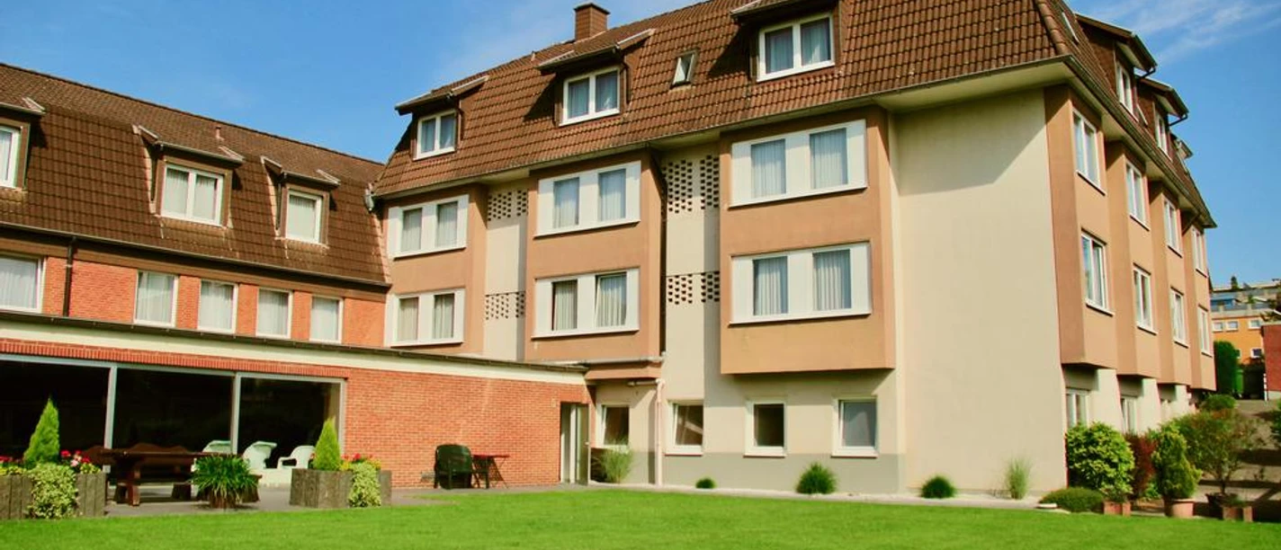 Hotel Fettehenne Dreistöckiges Gebäude mit braunem Dach und hellem Putz, umgeben von gepflegtem Garten.