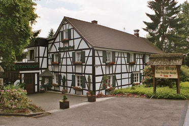 Aussenansicht Historisches Fachwerkhaus mit Blumenkästen, daneben ein Schild "Hotel Meyer, eine Bergische Gaststätte".