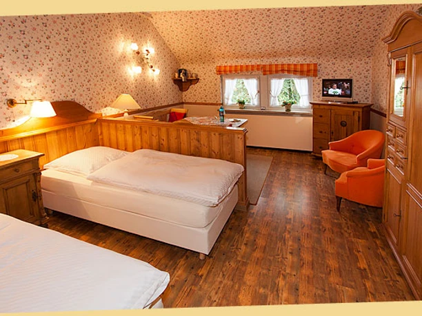 Doppelzimmer Bsp. 2 Gemütliches Gästezimmer mit floral tapezierten Wänden, zwei Betten, Holzmöbeln und warmem Licht.