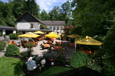 Hotel Rengser Mühle Ein idyllischer Gastgarten mit gelben Schirmen und Tischen vor einem charmanten zweistöckigen Gebäude.