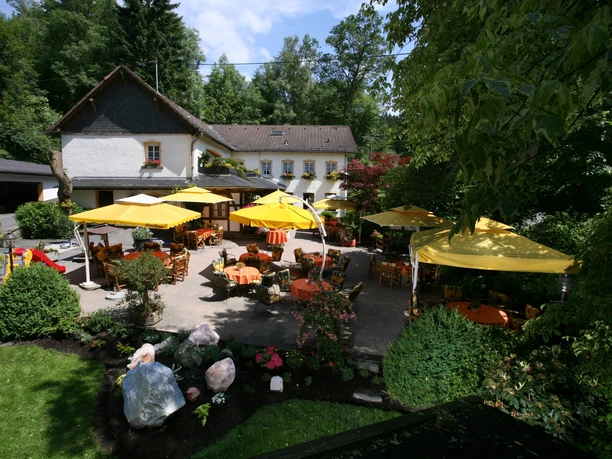 Hotel Rengser Mühle Ein idyllischer Gastgarten mit gelben Schirmen und Tischen vor einem charmanten zweistöckigen Gebäude.