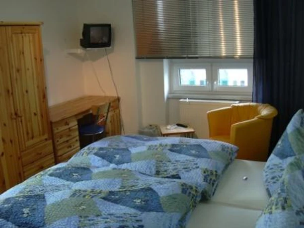 Zimmerbeispiel Doppelbett Ein gemütlich eingerichtetes Hotelzimmer mit Doppelbett, einem gelben Sessel und einem kleinen Fernseher.