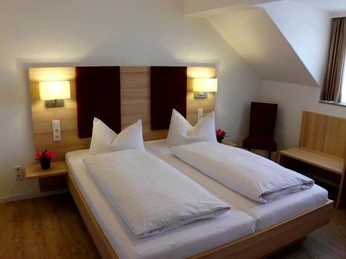 Zimmerbeispiel Doppelzimmer mit modernem Holzdesign, zwei Betten, Lampen und rot-braunen Akzenten an der Wand.