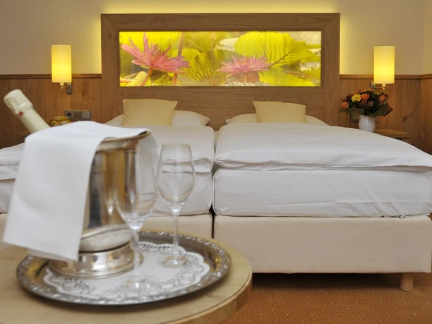 Gronauer Tannenhof Zwei Einzelbetten in einem Hotelzimmer, dekoriert mit gelben Kissen, Blumenbild an der Wand.