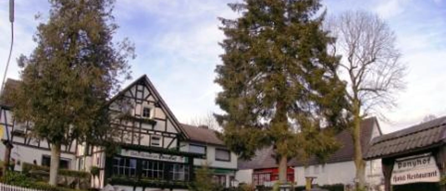 Außenansicht Fachwerkhaus mit Restaurant-Pension, umrahmt von Bäumen, unter blauem Himmel an einer Landstraße.