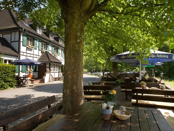 Biergarten - Terrasse Fachwerkhaus mit grünen Fensterläden, davor Biergarten mit Holzbänken und großen Sonnenschirmen.