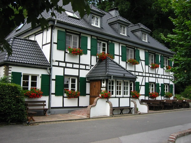 Hotelansicht Fachwerkhaus mit grünen Fensterläden und blühenden Geranien, gelegen an einer ruhigen Straße.