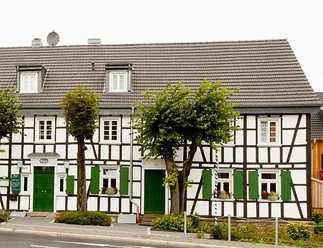 Hotel-Restaurant Zur Post - Biesfeld Fachwerkhaus mit dunkelbraunen Balken, weißen Wänden und grünen Türen, Fensterläden und Blumenkästen.