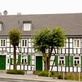 Hotel-Restaurant Zur Post - Biesfeld Fachwerkhaus mit dunkelbraunen Balken, weißen Wänden und grünen Türen, Fensterläden und Blumenkästen.