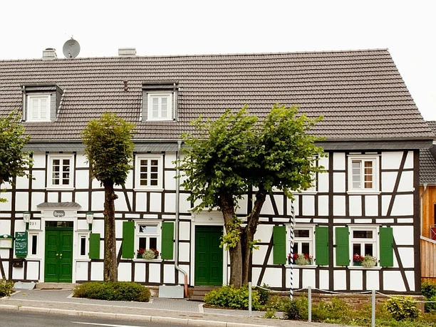 Hotel-Restaurant Zur Post - Biesfeld Fachwerkhaus mit dunkelbraunen Balken, weißen Wänden und grünen Türen, Fensterläden und Blumenkästen.