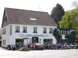 Hausansicht m. Motorrädern Ein zweistöckiges Gasthaus mit weißer Fassade, umgeben von geparkten Motorrädern und Bäumen.
