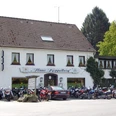 Hausansicht m. Motorrädern Ein zweistöckiges Gasthaus mit weißer Fassade, umgeben von geparkten Motorrädern und Bäumen.