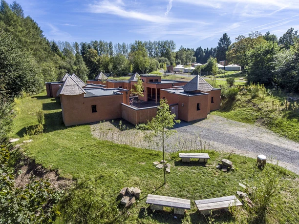 Jugendherberge Panarbora Rotes Gebäude mit Kegelspitzen, umgeben von grüner Wiese und Bäumen, unter blauem Himmel.