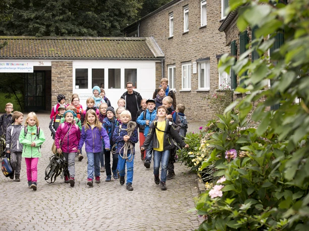 Jugendherberge Wipperfürth Eine Gruppe fröhlicher Schulkinder auf einem gepflasterten Hof vor einem Backsteingebäude.