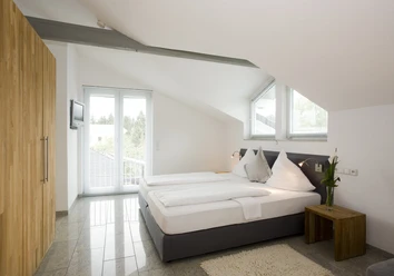 Doppelzimmer Helles Dachzimmer mit Doppelbett, Flachbild-TV an der Wand, großen Fenstern und Holzmöbeln.