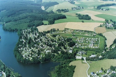 Campingplatz Lambacher Höhe Luftaufnahme eines Campingplatzes und Grünflächen an einem Seeufer, umgeben von Wäldern und Feldern.