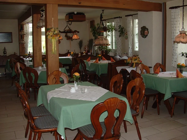 Restaurant Gemütlicher Gastraum mit grünen Tischdecken, hölzernen Stühlen und dekorativen Hängeleuchten.