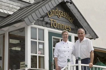 Landgasthof Tönnes Ein herzliches Paar vor dem Eingang eines charmanten Landgasthofs mit Holzverzierungen.