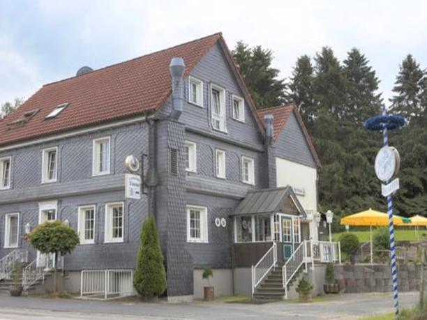 Landgasthof Tönnes Graues Fachwerkhaus mit rotem Dach, Außenterrasse mit gelben Sonnenschirmen, umgeben von Bäumen.