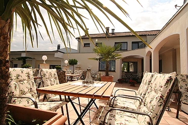 Landhotel Bergischer Hof Marialinden Sonniger Innenhof eines mediterranen Hauses mit gepolsterten Gartenstühlen und Palmen.