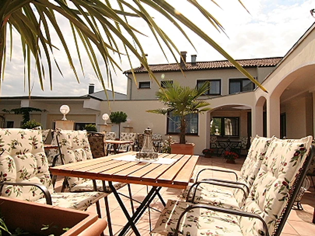 Landhotel Bergischer Hof Marialinden Sonniger Innenhof eines mediterranen Hauses mit gepolsterten Gartenstühlen und Palmen.